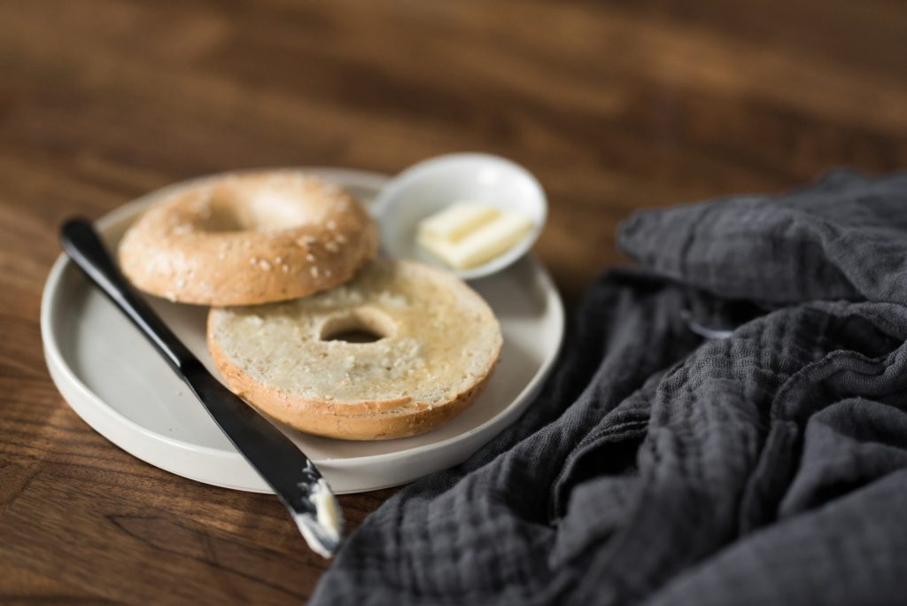 A bagel cut in half on a white plate on a wood surface.